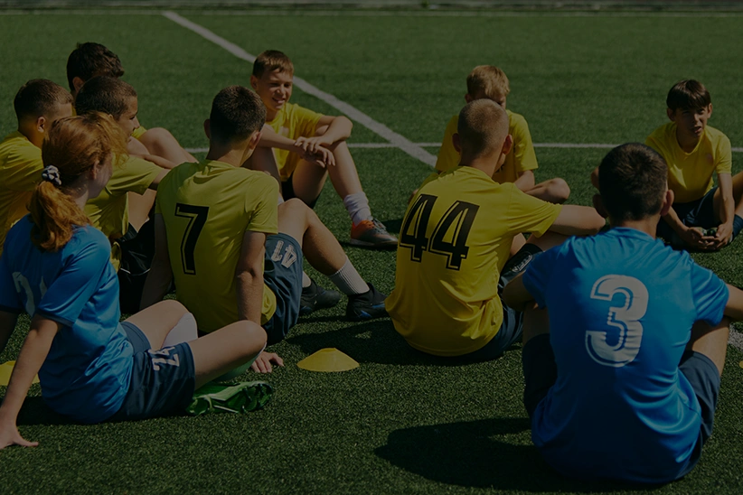 Children sitting on grass and listening to female football coach